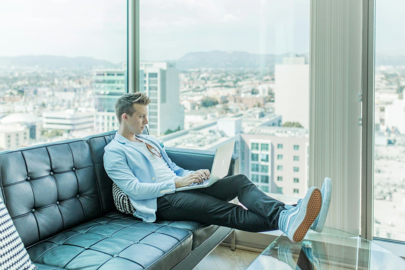 Someone working on a laptop from a couch overlooking a city skyline
